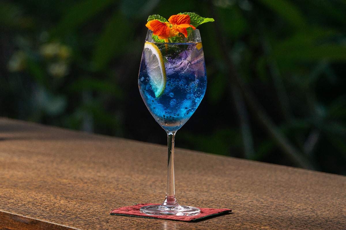 Refreshing blue cocktail garnished with mint leaves served on a wooden table during Happy Hours at Lebah Ubud Restaurant Bali