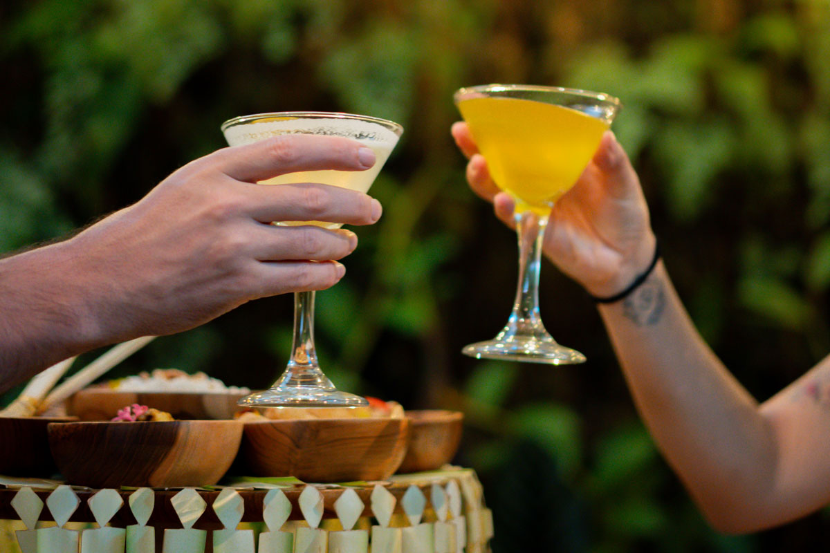 Hand holding a signature yellow cocktail glass in the tropical setting of Lebah Ubud Restaurant Bali
